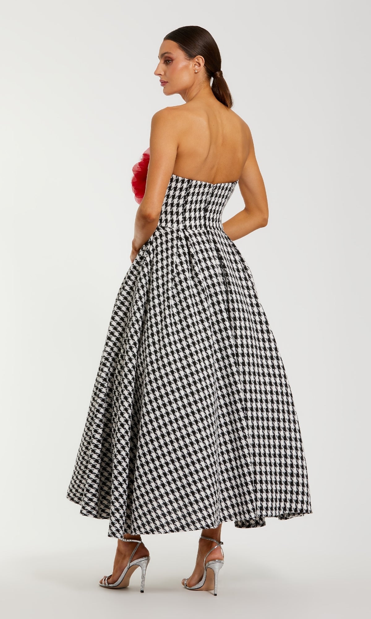 A woman stands facing away in the Mac Duggal 37068 Midi Hounds Tooth Formal Dress with a flared skirt and silver heels—a sophisticated option for formal events.